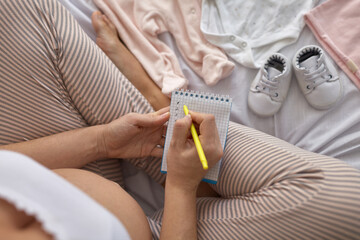 Fototapeta premium Top view of pregnant woman in the bed preparing baby clothes at home