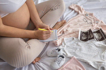 Top view of pregnant woman in the bed preparing baby clothes at home