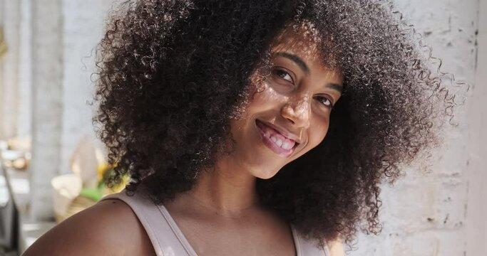 Very attractive biracial woman with a wide white-toothed smile, portrait in a stylish apartment. Alone at home, feels fine and confident. Freelancer blogger influencer close up.