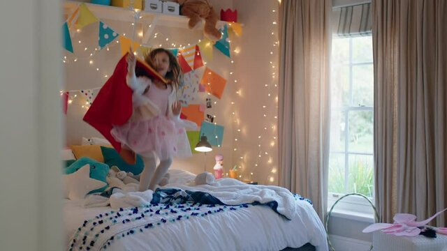 happy little girl jumping on bed wearing costume playing game enjoying playful imagination in colorful bedroom at home