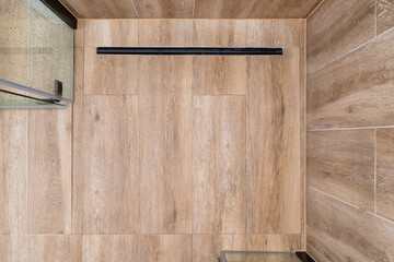 Modern black linear drain in a bathroom lined with ceramic tiles imitating wood, top view. - obrazy, fototapety, plakaty