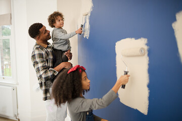 Happy father and children with paint rollers painting room