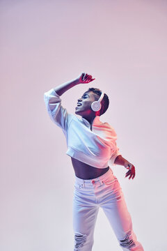 Active black dancer in headset dancing hip hop on light background