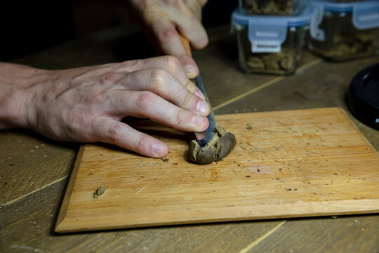 Crop man crushing dry marijuana piece on chopping board