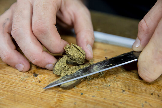 Crop man cutting dry marijuana piece on chopping board
