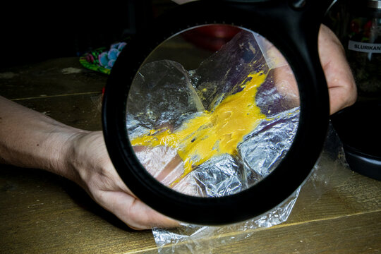 Crop man showing cannabis glue through magnifying light