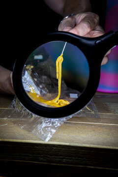 Crop person with cannabis glue on stick against magnifying lamp