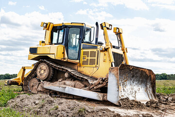 Bulldozer machine is leveling construction site. Earthmover with caterpillar is moving earth. Close-up. Construction heavy machinery.