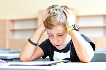 Bored, frustrated,stressed child  passing exam at school  sitting  alone at the table  at empty classroom.Learning difficulties, education concept.