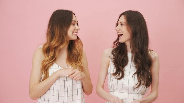 Smiling girls laughing to the camera standing isolated over pink background in the studio