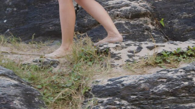 Brazilian girl walking barefoot at rocky beach, Balneário Camboriú, Brazil.
