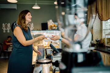 Choosing desserts. Middle age brunette beautiful successful pregnant woman standing near counter while buying delicious desserts in new bakery.