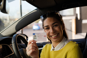 Portrait happy young woman holding new drivers license in car