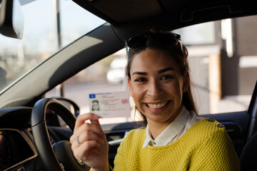 Portrait happy young woman holding new drivers license in car