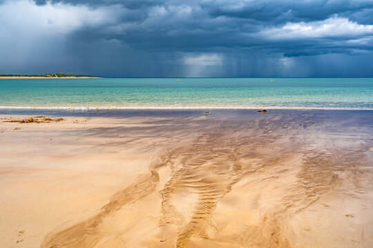 A small stream flowing out to sea over a sandy beach with dark storm clouds and rain over the ocean