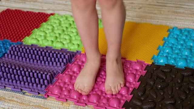 A child jumps on an orthopedic massage mat made of puzzles with surfaces of various shapes and tactility.  grass, cones, acorns - the texture of details. Prevention and treatment of flat feet