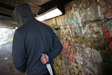 Obraz premium Dangerous man in hoody holding knife weapon in urban tunnel