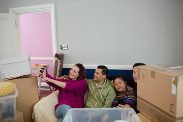 Happy friends taking a break from moving, taking selfie on sofa