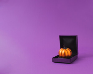 Shiny pumpkin in ring gift box for fun Halloween present concept. Purple and orange scheme.