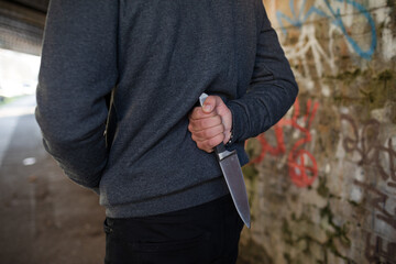 Dangerous man in hoody holding knife weapon in urban tunnel
