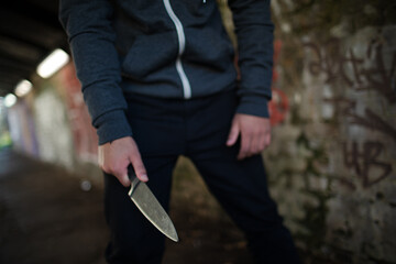 Dangerous man in hoody holding knife weapon in urban tunnel