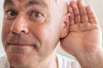 Fototapeta premium Close-up of a middle-aged Caucasian man with his hand on his ear to hear better. 