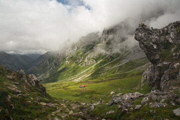 Collado del Frade en Picos de Europa. Idílico paisaje de montaña con cabaña en el centro rodeada de verdes prados con nubes alrededor de la montaña
