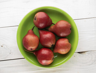 Several red pears in a ceramic plate on a wooden table, close-up, top view.