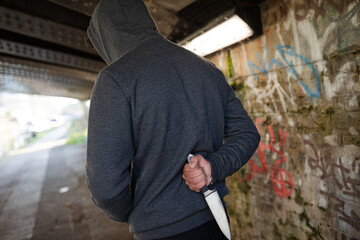 Dangerous man in hoody holding knife weapon in urban tunnel