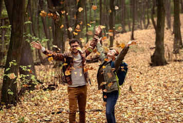 Two young hikers with backpack walking in forest and throwing leaves in the air.