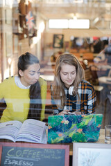 Young female college students studying at laptop in cafe window