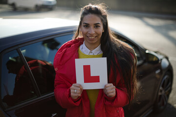 Portrait confident, happy young woman holding learners permit by car
