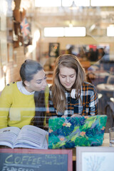 Young female college students studying at laptop in cafe window