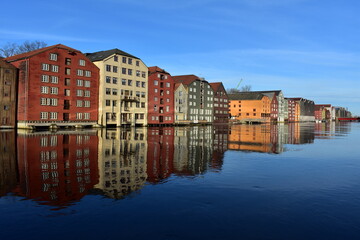  cityscape  of norwegian houses at the Bryggene  Trondheim near Nidelva riverin high tide.perspective colour houses refected in the water with blue sky