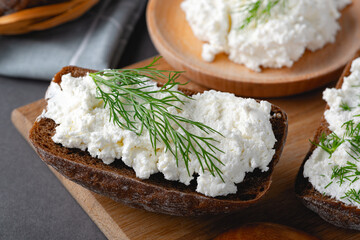 Home made rye bread on a wooden cutting board with curd cheese, ricotta and dill