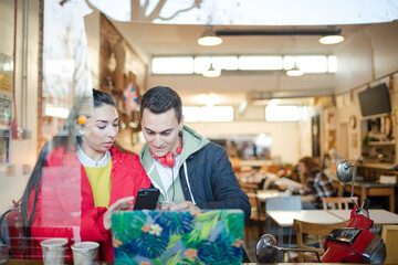 Obraz premium Young couple using smart phone and laptop in cafe