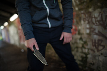 Dangerous man in hoody holding knife weapon in urban tunnel