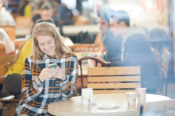 Smiling young woman using smart phone in cafe