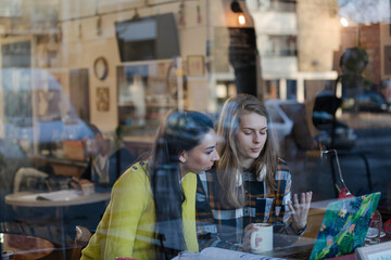Young female college students studying at laptop in cafe window