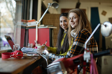 Portrait smiling female college students studying at laptop in cafe