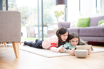 Sisters using digital tablet on living room floor