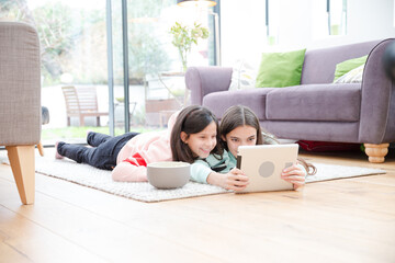 Sisters using digital tablet on living room floor