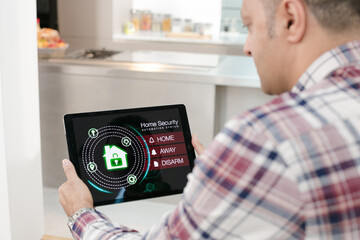 Man setting smart home alarm system from digital tablet on living room sofa