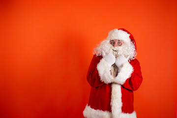 Funny cheerful santa claus points his hands to the side. A man in a Christmas costume on an orange background.