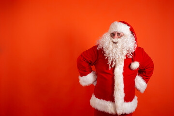 Funny cheerful santa claus points his hands to the side. A man in a Christmas costume on an orange background.