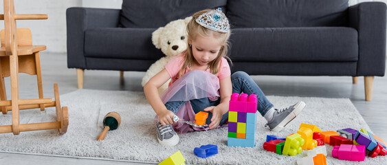 child in princess costume playing with magic wand and colorful building blocks on floor, banner