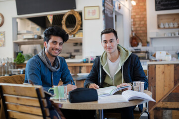 Portrait confident young male college students studying at cafe table