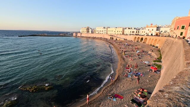 Incredible sunset shots of the beach of Gallipoli, the heart of Salento in Puglia. Italy. People take a bath enjoying the coolness of the late afternoon sun. In the background the village.
