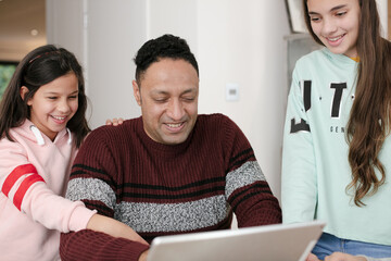 Father and daughters using digital tablet in morning kitchen