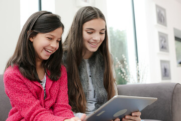 Happy sisters using digital tablet on living room sofa